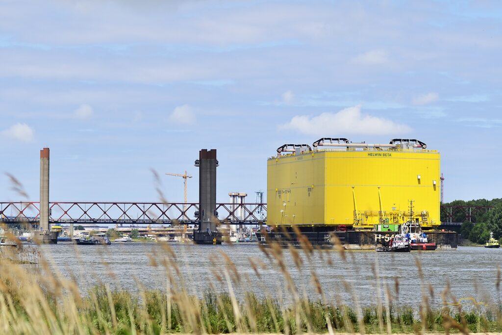 Groot geel offshoreplatform, Helwin Beta, op een schip dat over een rivier wordt gesleept. | fotograaf Spijkenisse